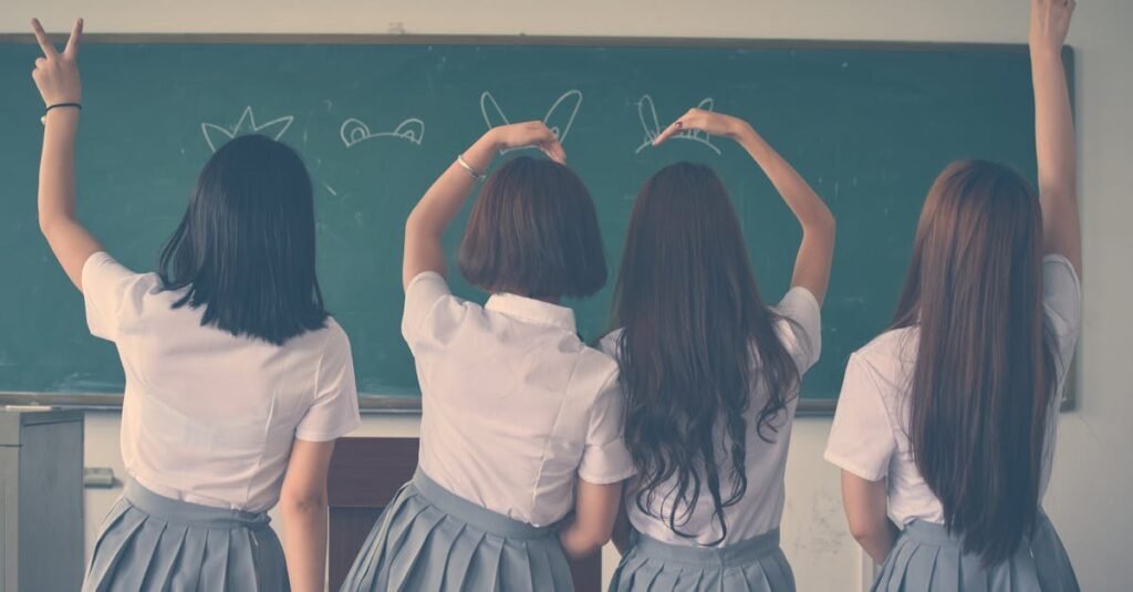Group of teenage girls in school uniforms enjoying time together in a classroom, posing with playful gestures.