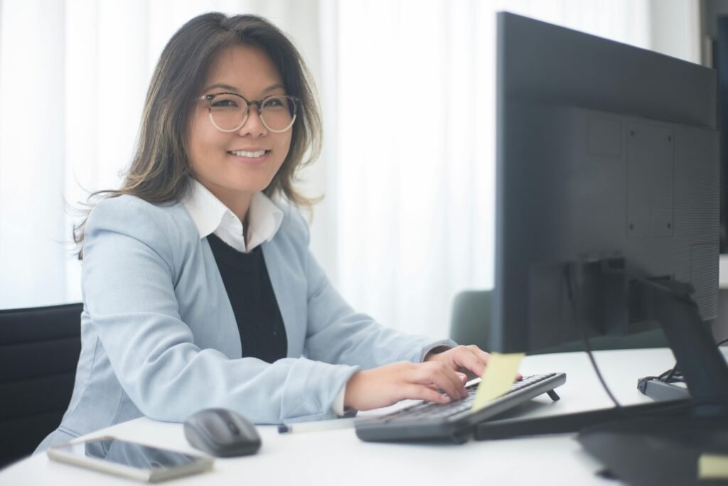 Professional woman smiling while working at a computer in an office setting.